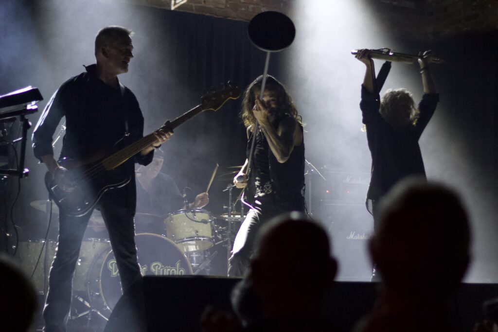 Deeper Purple performing live on stage with audience silhouettes in foreground