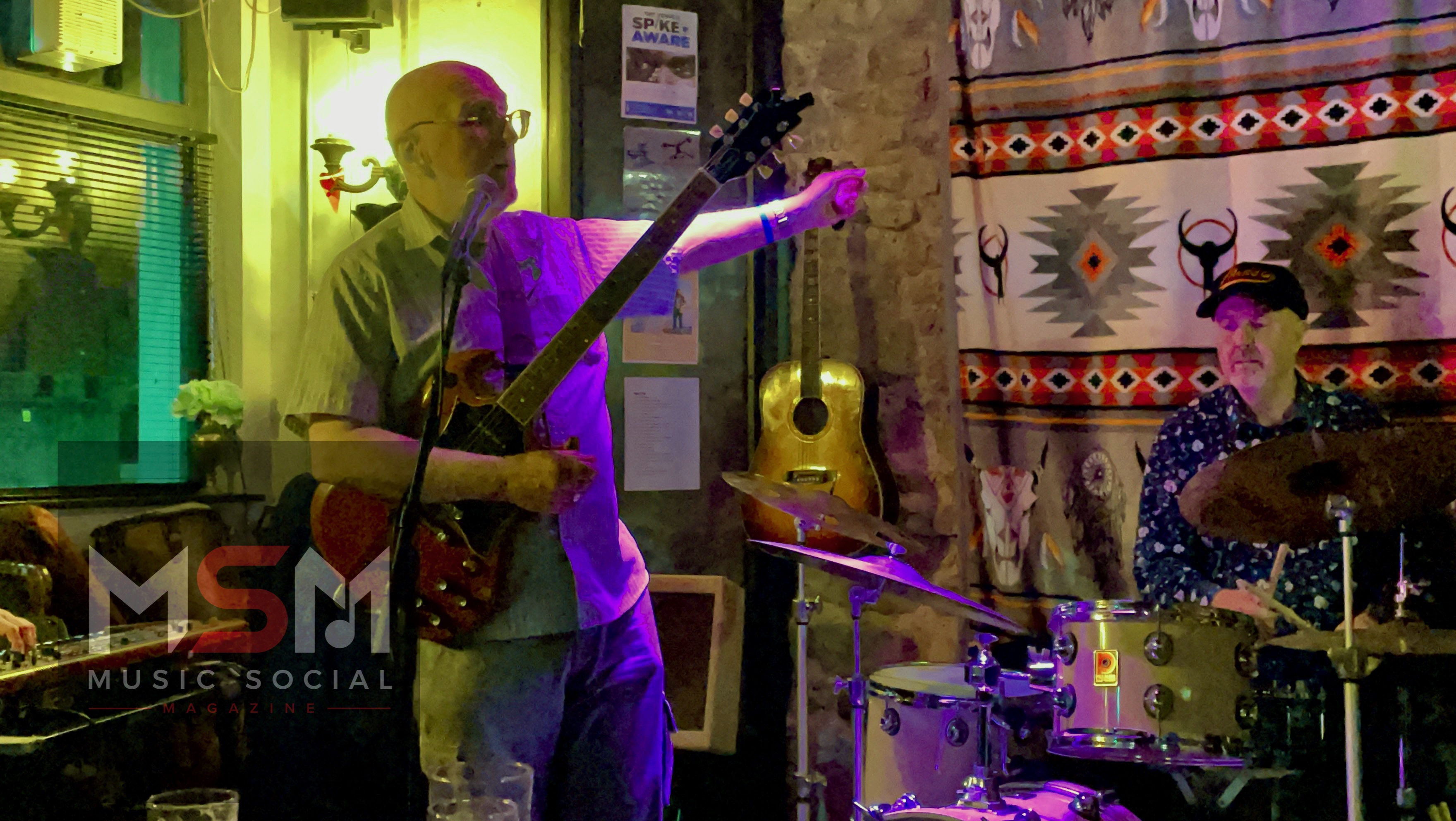 Pete performing on guitar during The Blues Social at The Platform Tavern in Southampton, with drummer Mike behind him under colourful stage lighting.