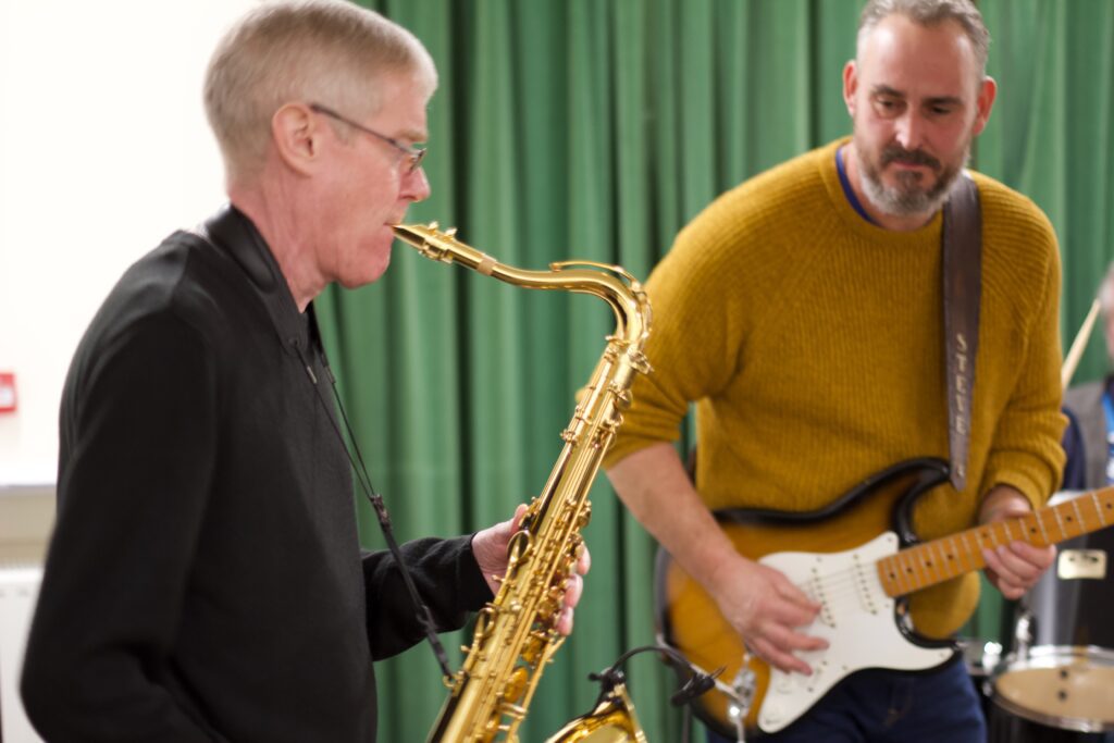 Paul Tasker on saxophone and Steve Brennan on guitar performing together with Chicago 9 during a live performance.