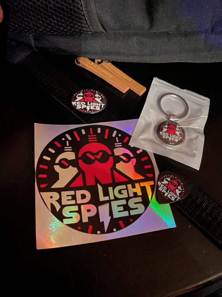 Red Light Spies merchandise including stickers, badges and a keyring presented to Music Scene Magazine after the band's performance at The Stage Door, June 2026.