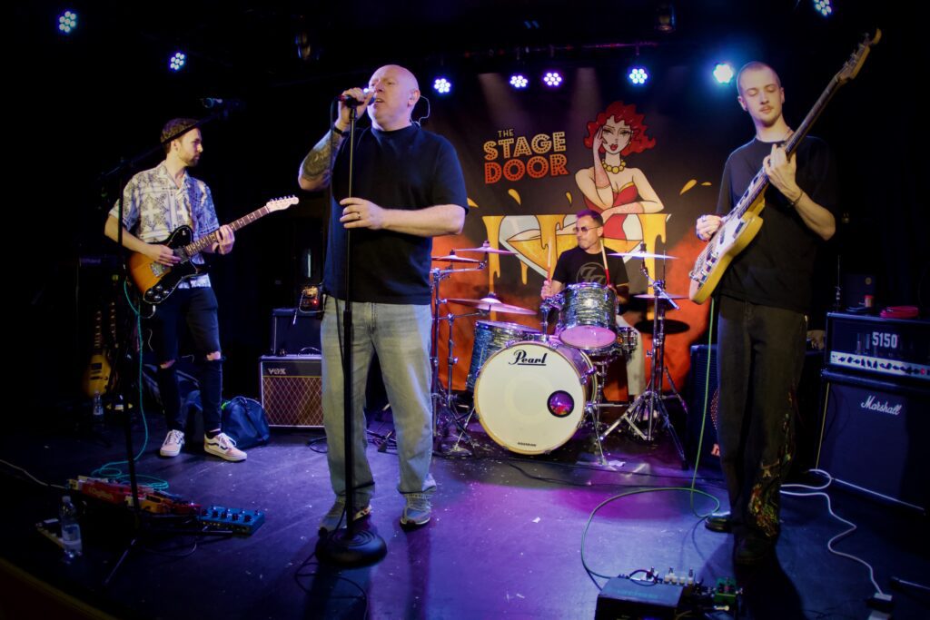 Red Light Spies performing live at The Stage Door in Southampton during the RSTE Promotions Launch Party with blue stage lighting, June 2026.